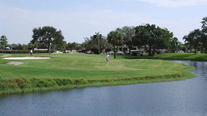 006 - A scenic view on a Vista Plantation golf course with a water hazard on the right, a bunker on the left, and players in the distance under a clear blue sky_
