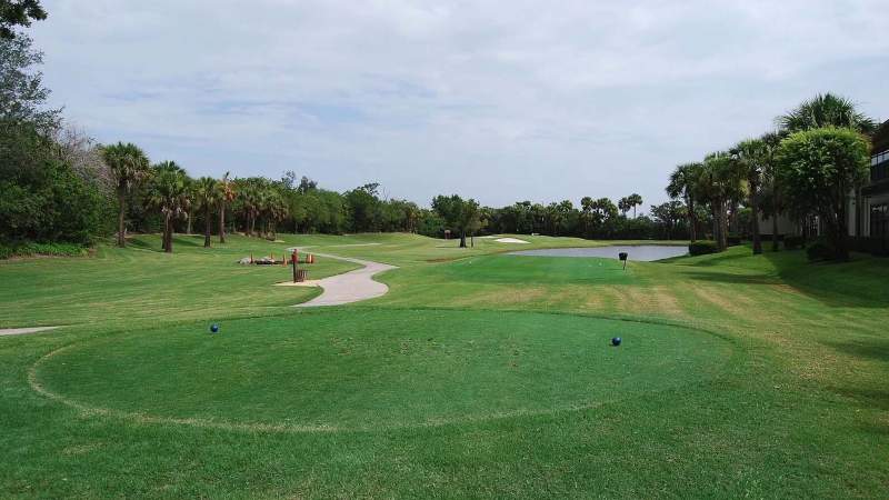 023 - A serene Vista Plantation golf course with a lush green fairway, a water hazard on the right, and surrounding palm trees under a cloudy sky_