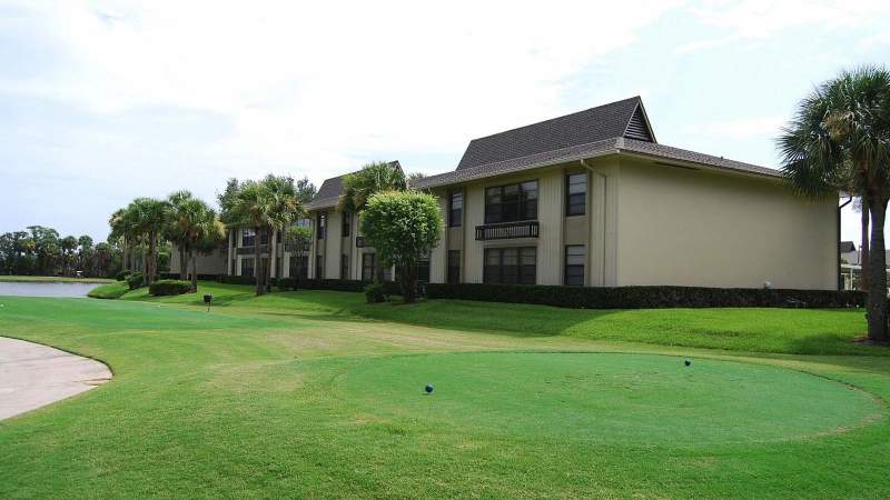 025 - A golf course with a green lawn and a pathway in front of a Vista Plantation multi-story residential building under a clear sky_